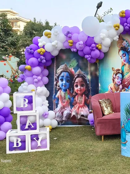 A close-up of the Krishna-themed backdrop with "BABY" blocks and a pink sofa for seating.
