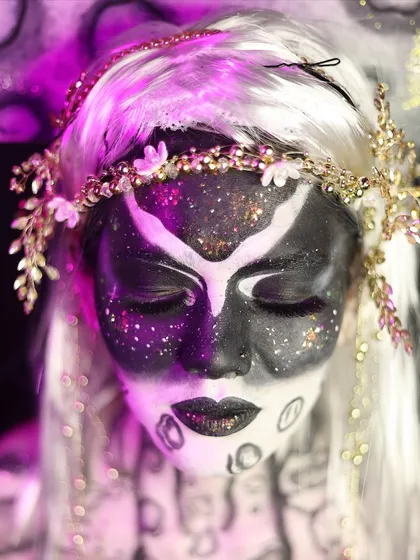 A close-up of a mystical, celestial being with black and white body paint and a galaxy of glitter. This is an example of advanced fantasy makeup.