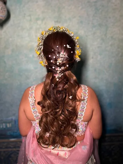 The back of this beautiful Haldi hairstyle. I created a half-updo with a pearl-adorned braid and let the rest of the hair flow in soft curls, crowned with a fresh floral tiara.