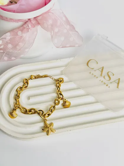 This styled shot features a gold charm bracelet with sea-themed charms. The simple, elegant setup with the brand's packaging is great for social media and online stores.