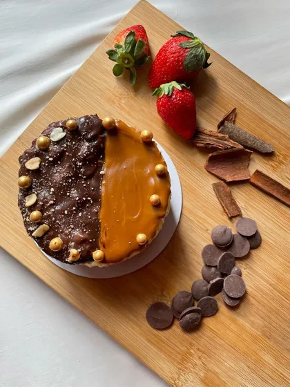 The best of both worlds. This eggless New York cheesecake features a split topping of chocolate-peanut and salted caramel, beautifully presented on a wooden board with fresh ingredients.