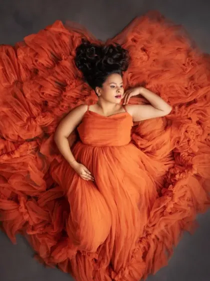 A portrait of pure love. This overhead shot showcases the artistry of our gown styling, with a vibrant orange tulle dress arranged in a perfect heart shape to beautifully frame you and your bump.