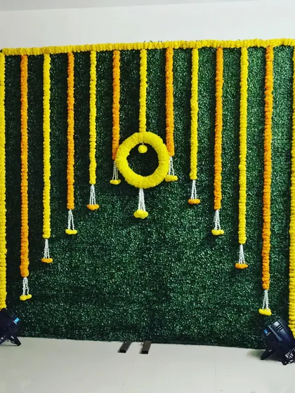 Sometimes, simplicity is the most elegant. This backdrop uses a green turf wall adorned with hanging garlands of yellow and orange marigolds, offering a clean and traditional look for any puja or ceremony.