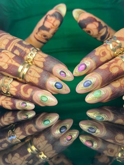 A truly unique design featuring nails that look like precious gems, with colorful stones set within a gold-outlined frame, shown against henna-adorned hands.