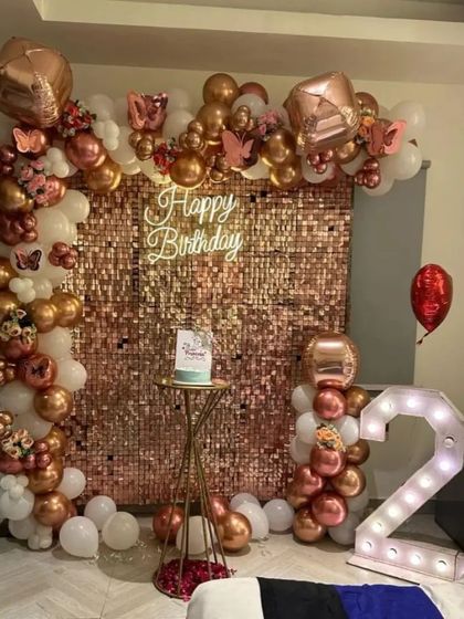 A full view of a luxurious 21st birthday bedroom decoration. The rose gold sequin wall is the centerpiece, framed by a matching balloon arch and complemented by '21' marquee lights.