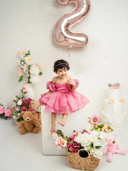Sitting pretty for her second birthday portrait. Dressed in a lovely pink gown, she is surrounded by flowers and a rose gold '2' balloon, creating a picture-perfect memory.