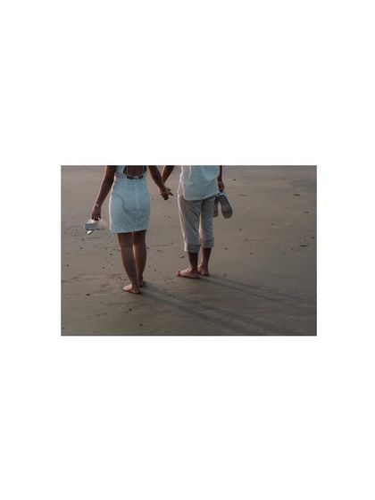A simple, minimalist shot of the couple walking away on the sand, shoes in hand. The focus is on their journey together.