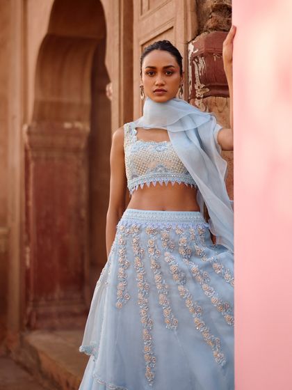 A portrait focusing on the unique neckline and detailed embroidery of a powder blue blouse. The styling is clean and fresh, letting the craftsmanship of the outfit take center stage.
