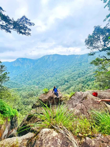 A trekker sits on a rock, taking in the vast green landscape. Our trips offer moments of quiet contemplation amidst the group fun.