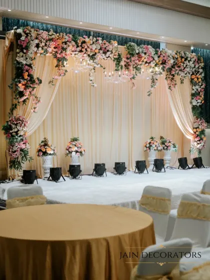 For a classic and elegant reception, I designed this stage with a lush floral arch over soft, draped fabric. Spotlights and elegant floral urns complete the look, creating a timeless space for celebration.
