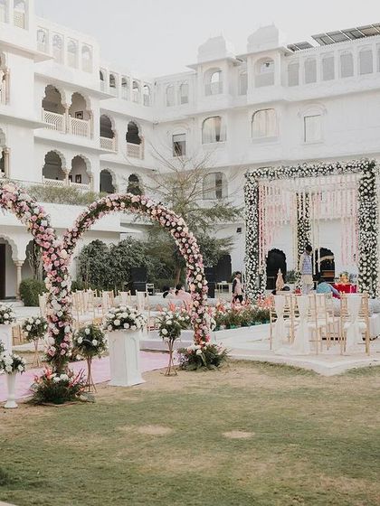 The full view of the palace courtyard wedding, with heart-shaped floral arches leading the way to the beautiful white floral mandap.