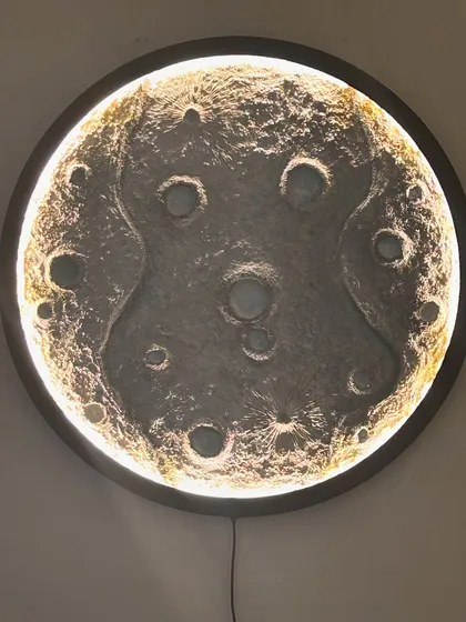 The black-framed moon lamp, glowing warmly. The light creates beautiful shadows in the craters, making it look incredibly realistic.