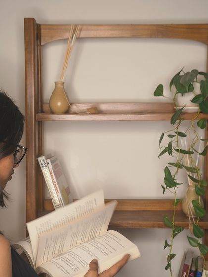 This image captures the experience of using the bookshelf, creating a personal library corner in your home. The solid teak construction ensures it will be a part of your story for years.