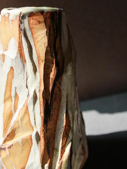 A close-up of the tall Kurinuki vase, showing the intricate details of the carved surface. The process is meditative, a slow reveal of the form within the clay.