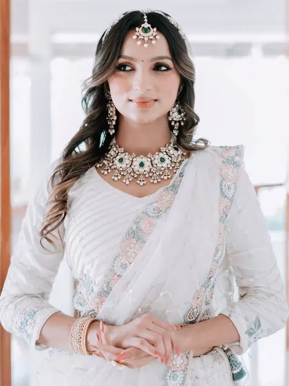An elegant and serene look. This model wears a white saree with a beautiful kundan and green bead necklace, a sheeshpatti, and matching earrings, ideal for a daytime wedding or festive puja.