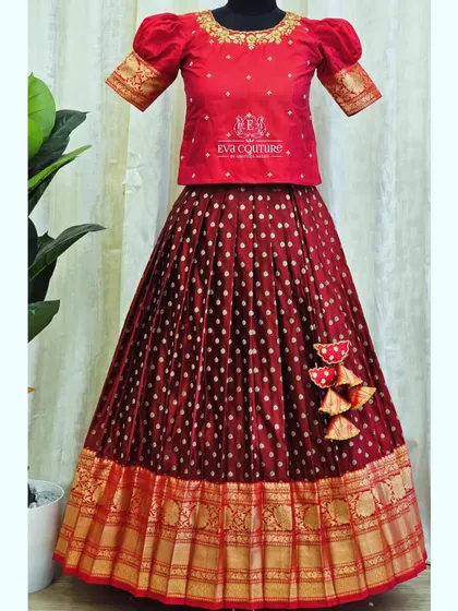 A classic maroon and gold combination. This Pattu Pavadai features a simple embroidered blouse and a skirt with butti work and a traditional zari border.