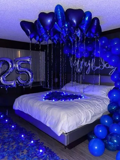 A bold and striking room decoration in deep blue and silver. This premium setup includes heart-shaped foil balloons, large number balloons for a 25th birthday, and dramatic lighting.