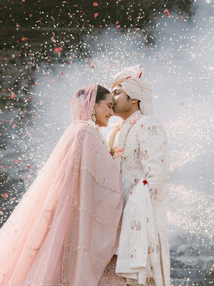 A moment of magic and celebration. The groom kisses his bride's forehead as fireworks light up the background, creating a truly cinematic and unforgettable portrait of their love.