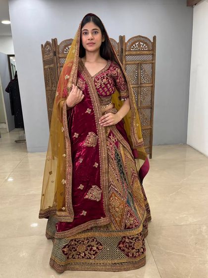 A full view of a magnificent multi-toned velvet bridal lehenga. The combination of deep maroon, green, and gold gives it a unique and regal appearance, available as a pre-loved treasure.