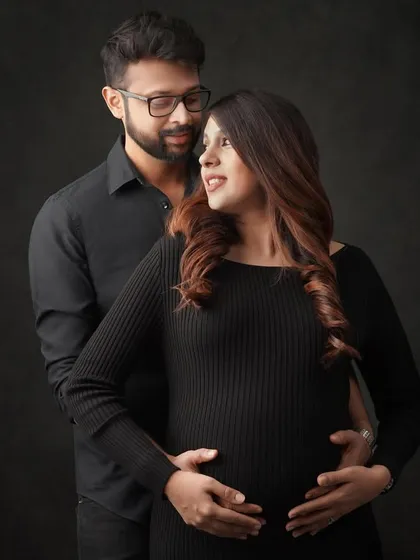 A classic pose for a couple's maternity session against a dark, moody backdrop. This style creates a feeling of intimacy and timeless elegance, focusing on the connection between the partners.