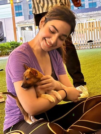 A participant sits on the grass, smiling as she cuddles a small brown puppy in her arms during an outdoor Pawga event.