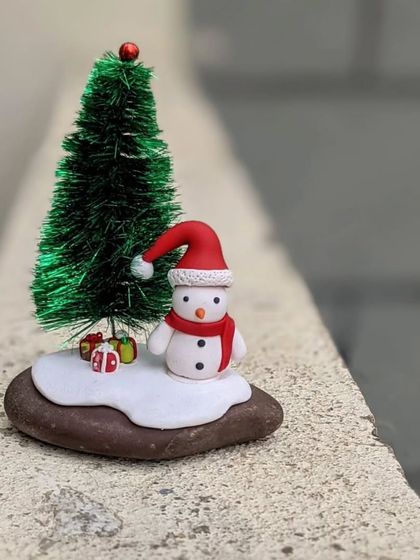 A miniature snowman scene on a natural stone, complete with a tiny Christmas tree and gifts.
