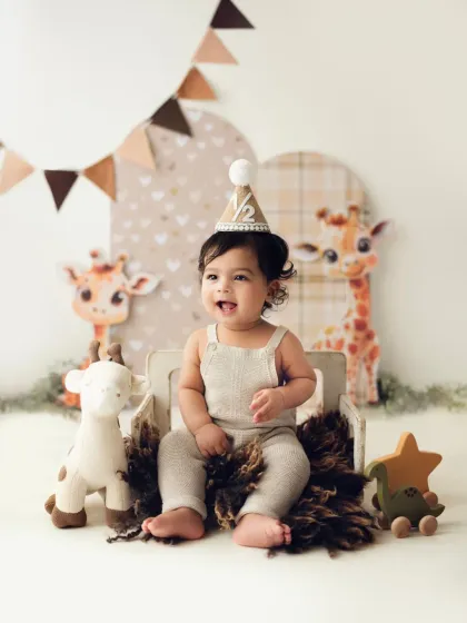 A joyful baby boy in his half-birthday hat, surrounded by cute giraffe props and earthy tones.