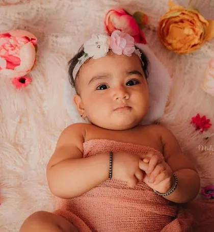This pretty 8-month-old is wrapped in a peach swaddle, surrounded by flowers. A beautiful, soft setup for a milestone shoot.