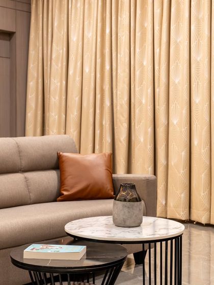 A detail shot of the lounge area, featuring a nested coffee table with both marble and stone tops. The textures of the sofa fabric, leather cushion, and patterned curtains come together to create a layered and tactile experience.