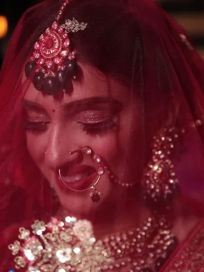 A close-up bridal portrait under the veil. The soft red light and focus on the bride's eyes and jewelry create a dreamy and romantic image.