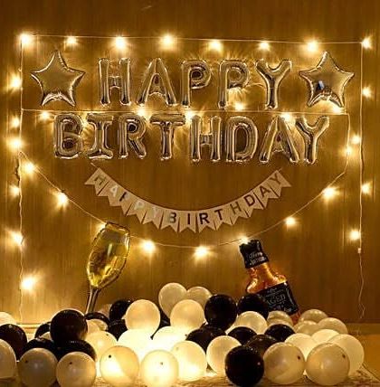 A stylish birthday setup for an adult, featuring black and white balloons, fairy lights, and props like a champagne glass and bottle.