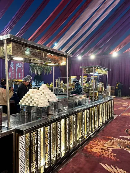 Another angle of the dessert station, showing the stacks of sweets ready for guests. The setup under the tent with purple draping creates a rich and celebratory atmosphere.