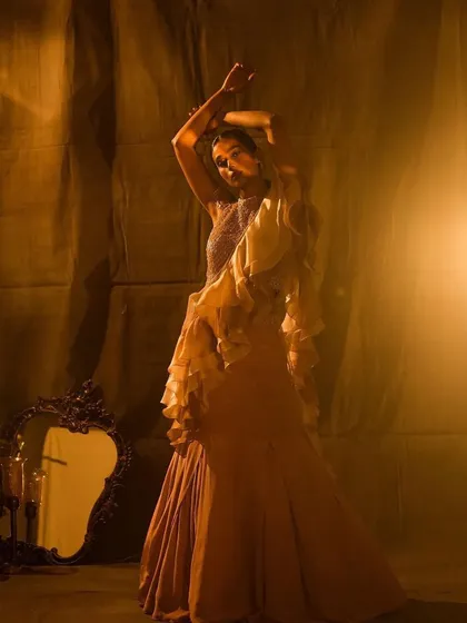 A full-length pose showcasing a dramatic ruffled saree. The makeup is kept elegant and understated to balance the volume of the outfit, with a focus on a flawless complexion and defined features.
