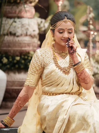 A stunning bride in an ivory and gold saree, her pose delicately showcasing her intricate mehendi.