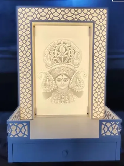 A compact and artistic mandir design featuring a detailed, paper-cut style portrait of a deity. The frame and base have a simple jali pattern, showing our versatility in creating personalized and unique sacred spaces.