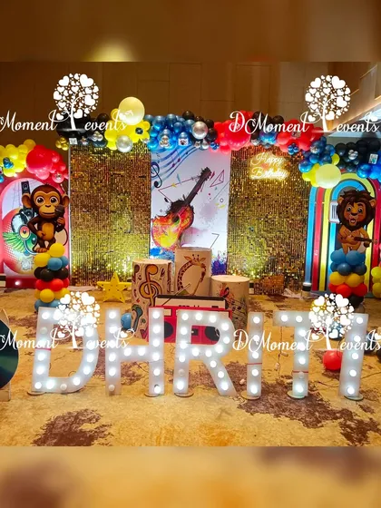 A vibrant and energetic Musical-themed first birthday stage. The decor features a sequin backdrop, musical note cutouts, a large guitar graphic, and fun animal characters playing instruments.