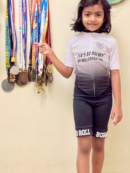 A young champion proudly pointing to her medals while sporting our professional academy gear.