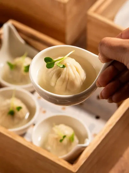 A hand lifting a delicate soup dumpling, ready to be eaten. This shot is all about capturing that "can't wait to eat this" moment.