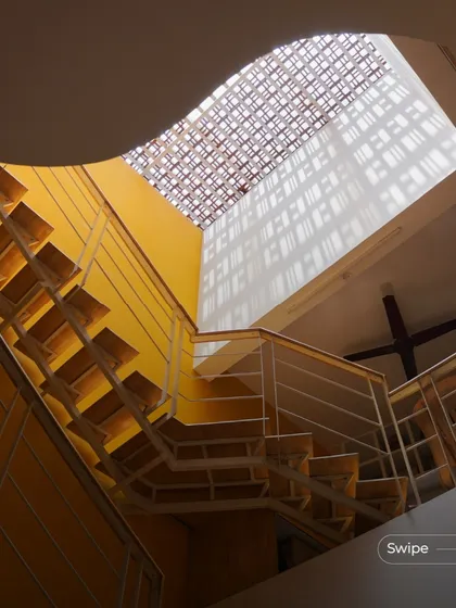 The floating metal staircase in the Raghavendra Residence, set against a bright yellow wall and lit from above by a patterned skylight, creates a stunning vertical element in the home.
