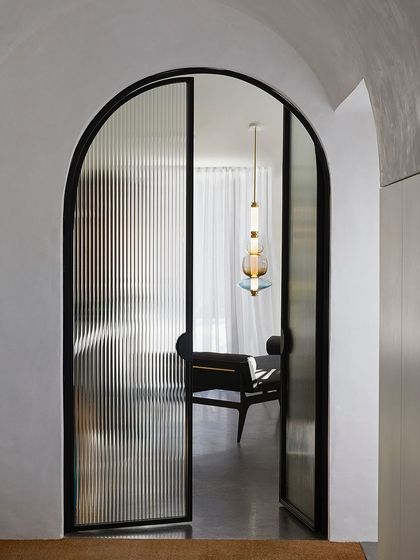 Viewed through an arched doorway with reeded glass, a Luna pendant offers a tantalizing glimpse of the beautifully lit space beyond.
