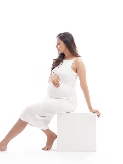 A simple and modern pose using a white block, this shot highlights the beautiful silhouette of pregnancy. The clean, minimalist background keeps the focus entirely on the mother-to-be.