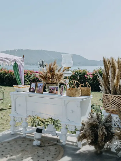A memory station set against a stunning lakeside view. A vintage-style white console table was used to display the couple's photos, surrounded by pampas grass for a soft, romantic feel.