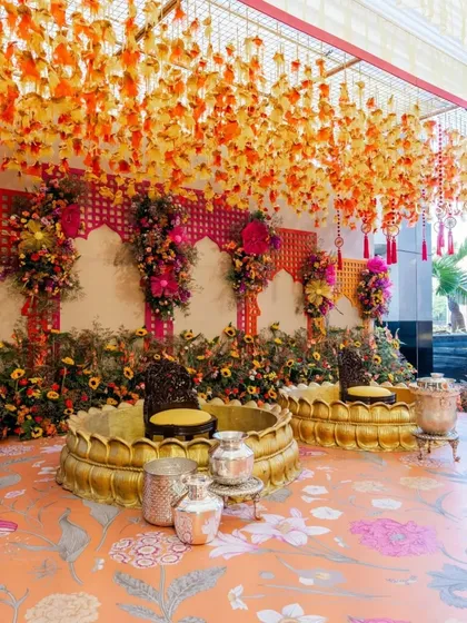 A beautiful seating area for the haldi ceremony. The golden lotus-shaped seats are surrounded by sunflowers and other floral arrangements, with a patterned floor adding to the festive design.