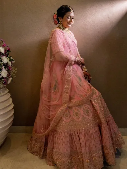 The full view of this bride's dreamy pink lehenga look. The soft makeup and floral hair accessories create a romantic and ethereal vibe.