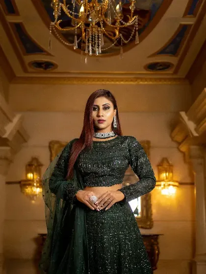 A powerful and stylish portrait of a bride in a dark green lehenga. The low-angle shot and grand hallway create a sense of drama and confidence.