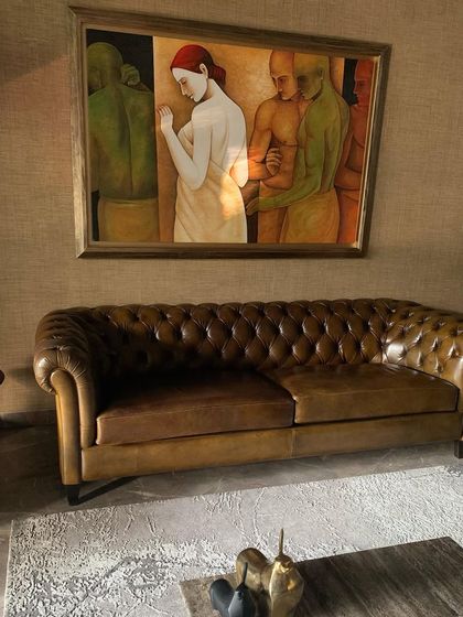 A classic tufted Chesterfield sofa in brown leather, set against a textured wall and a powerful piece of figurative art.