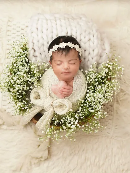 An overhead shot of a swaddled newborn in a basket, creating the look of a beautiful gift. The arrangement of flowers and soft fabrics makes for a truly artistic newborn photo.