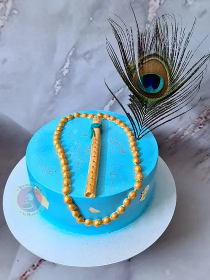 An elegant Janmashtami cake with a fondant flute and a string of golden beads.
