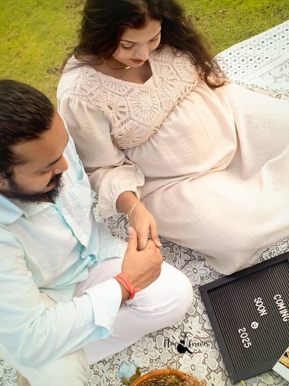 An overhead view of the couple holding hands, with their announcement board and sonogram pictures nearby. This angle provides a unique perspective on their special picnic.
