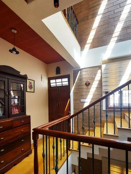 Light from a high window illuminates a hallway and staircase, showcasing the rich tones of the wooden furniture and the texture of the mud block walls.